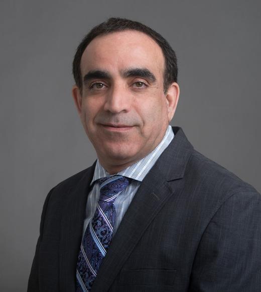 A man in a suit with a patterned tie stands against a gray background